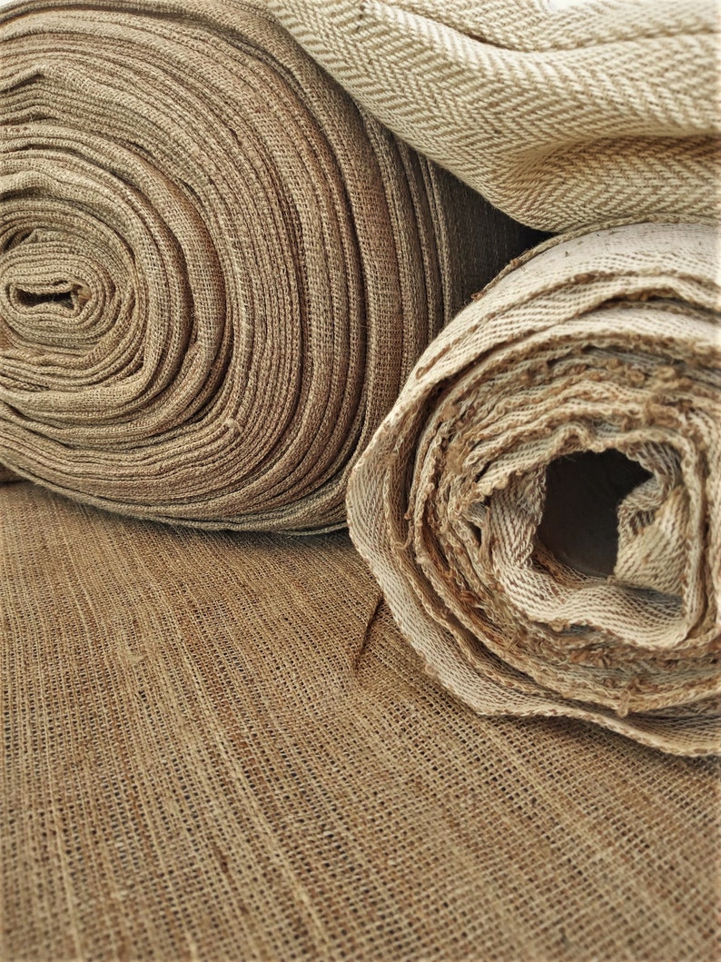 May include: Three rolls of brown burlap fabric, two are rolled up and one is unrolled. The fabric has a woven texture.