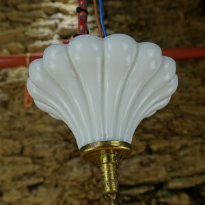 May include: A white glass lampshade with a scalloped edge hangs from a gold metal fixture. The lampshade is shaped like a seashell.