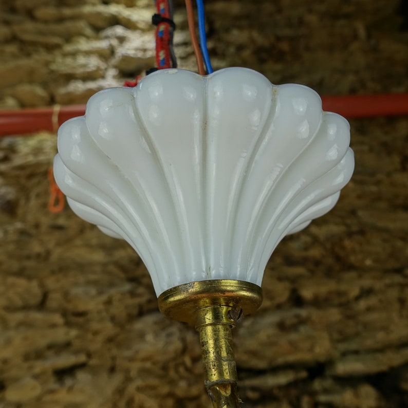 May include: A white glass lampshade with a scalloped edge hangs from a gold metal fixture. The lampshade is shaped like a seashell.