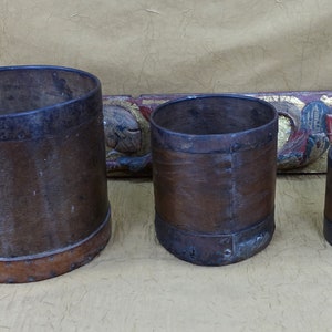 May include: Three brown leather-wrapped metal containers of varying sizes. The containers have a rustic, antique look and are lined with metal bands.