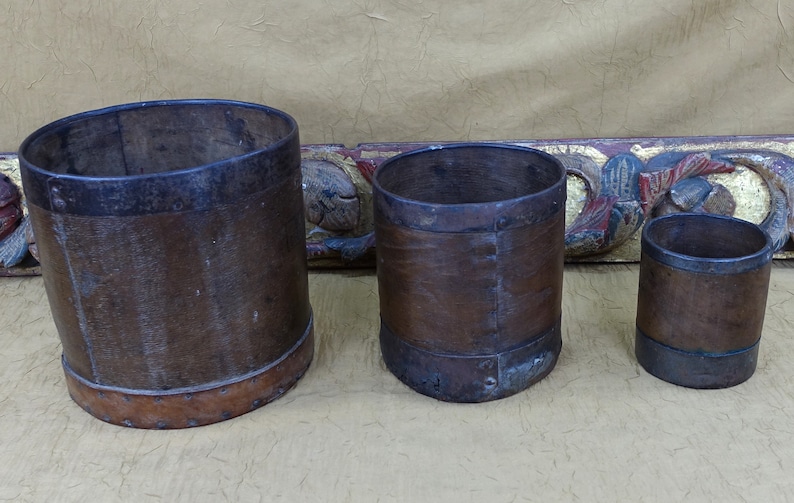 May include: Three brown leather-wrapped metal containers of varying sizes. The containers have a rustic, antique look and are lined with metal bands.