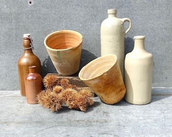 May include: A collection of five vintage pottery items, including two brown glass bottles, two terracotta pots, and a white ceramic jug. The items are arranged on a gray textured surface.