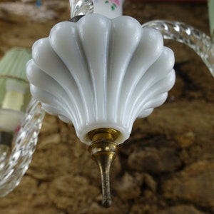 May include: A white glass chandelier shade with a scalloped edge and a gold metal finial. The shade is attached to a clear glass arm.