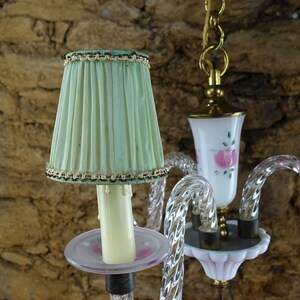 May include: A vintage chandelier with a green fabric lampshade and a white glass shade with pink roses. The chandelier is made of clear glass and has a crystal-like design.