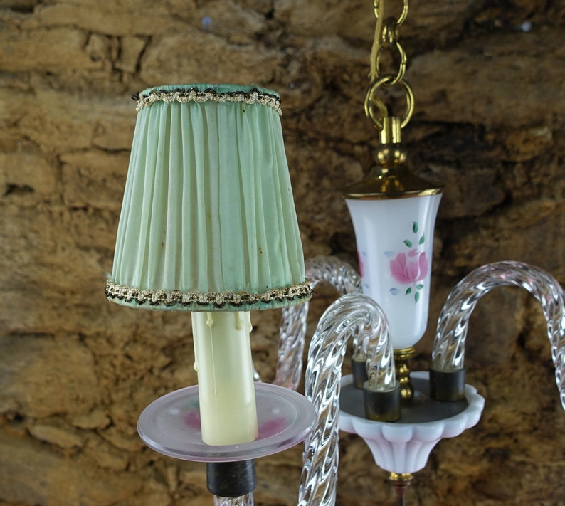 May include: A vintage chandelier with a green fabric lampshade and a white glass shade with pink roses. The chandelier is made of clear glass and has a crystal-like design.