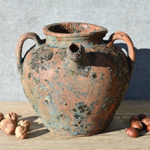 Pu&ograve; includere: Un grande vaso in terracotta rustico con un beccuccio e due manici. Il vaso ha una smaltatura blu e marrone screziata e mostra segni di et&agrave; e usura.