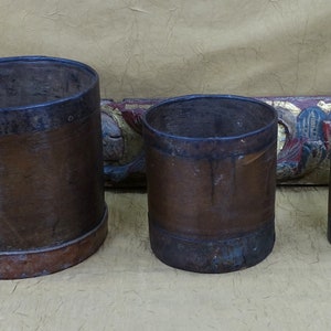 May include: Three brown wooden buckets with metal bands around the top and bottom. The buckets are different sizes and are arranged from largest to smallest.