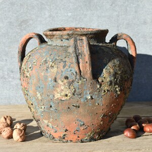 Pu&ograve; includere: Un grande vaso in terracotta rustico con due manici e una finitura usurata, screziata di blu e marrone. Il vaso ha un corpo arrotondato e un'ampia apertura.