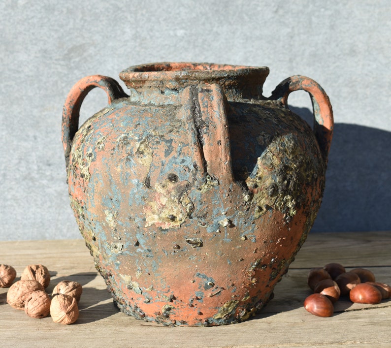 Pu&ograve; includere: Un grande vaso in terracotta rustico con due manici e una finitura usurata, screziata di blu e marrone. Il vaso ha un corpo arrotondato e un'ampia apertura.