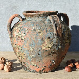 Pu&ograve; includere: Un grande vaso in terracotta rustico con due manici. Il vaso ha una finitura usurata e invecchiata con una patina blu-verde, perfetto per aggiungere un tocco di fascino vintage al tuo arredamento.