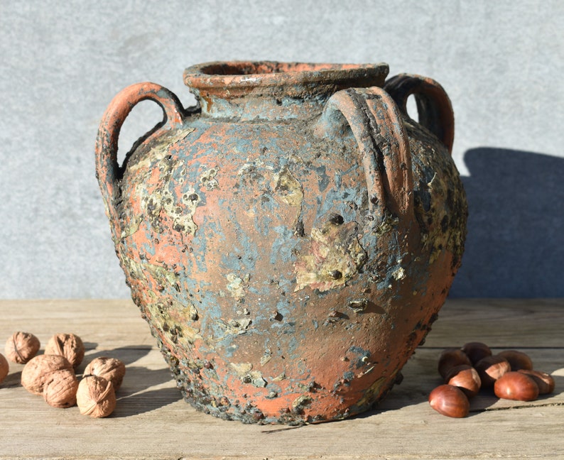 Pu&ograve; includere: Un grande vaso in terracotta rustico con due manici. Il vaso ha una finitura usurata e invecchiata con una patina blu-verde, perfetto per aggiungere un tocco di fascino vintage al tuo arredamento.