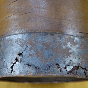 May include: Close-up of a wooden object with a metal band around the bottom. The metal band is cracked and shows signs of rust.