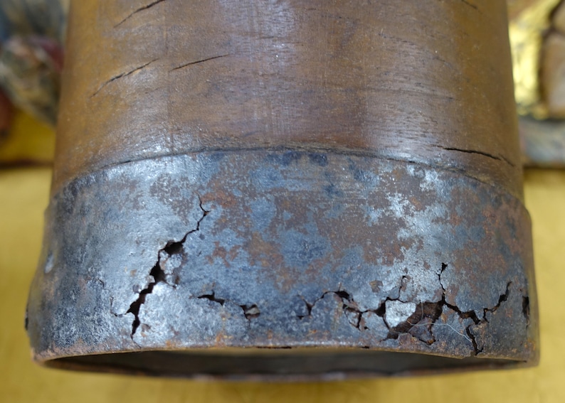 May include: Close-up of a wooden object with a metal band around the bottom. The metal band is cracked and shows signs of rust.