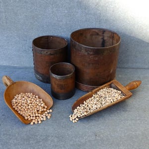 Peut inclure: Ensemble de tasses et de cuillères à mesurer en bois antiques. Deux cuillères sont remplies de pois chiches et de haricots blancs. Les tasses sont de tailles variées et ont des bandes métalliques. Les articles sont disposés sur une surface grise.