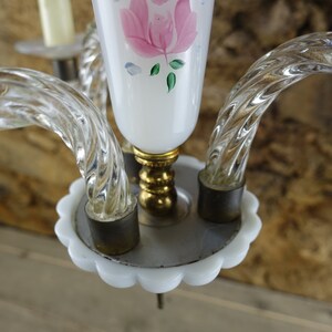 May include: A white glass chandelier with three clear glass arms and a white base with a scalloped edge. The chandelier has a pink rose painted on the center glass shade.