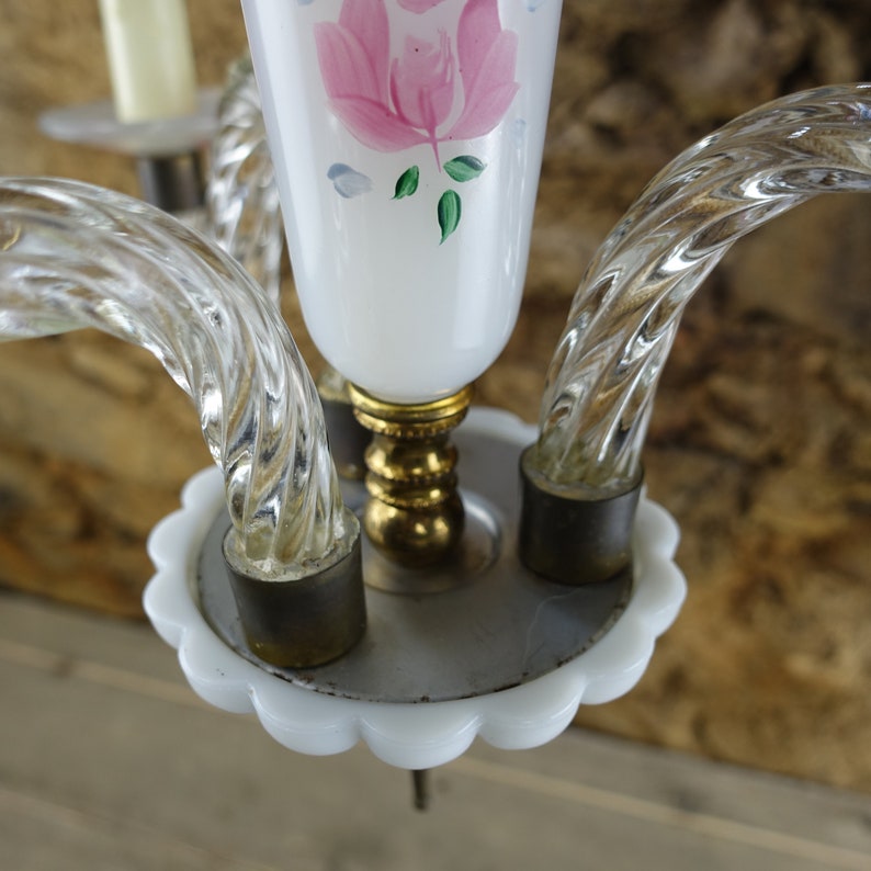 May include: A white glass chandelier with three clear glass arms and a white base with a scalloped edge. The chandelier has a pink rose painted on the center glass shade.