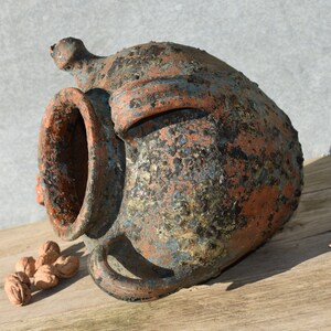 Pu&ograve; includere: Un grande vaso in terracotta rustico con un'ampia apertura e una superficie ruvida e testurizzata. Il vaso &egrave; ricoperto da uno strato di patina blu-verde, che gli conferisce un aspetto invecchiato e usurato.