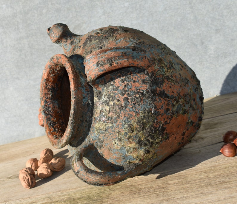Pu&ograve; includere: Un grande vaso in terracotta rustico con un'ampia apertura e una superficie ruvida e testurizzata. Il vaso &egrave; ricoperto da uno strato di patina blu-verde, che gli conferisce un aspetto invecchiato e usurato.