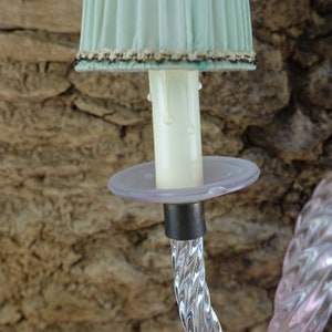 May include: A crystal chandelier arm with a frosted glass candle holder and a pale green lampshade. The candle holder has a white wax drip.