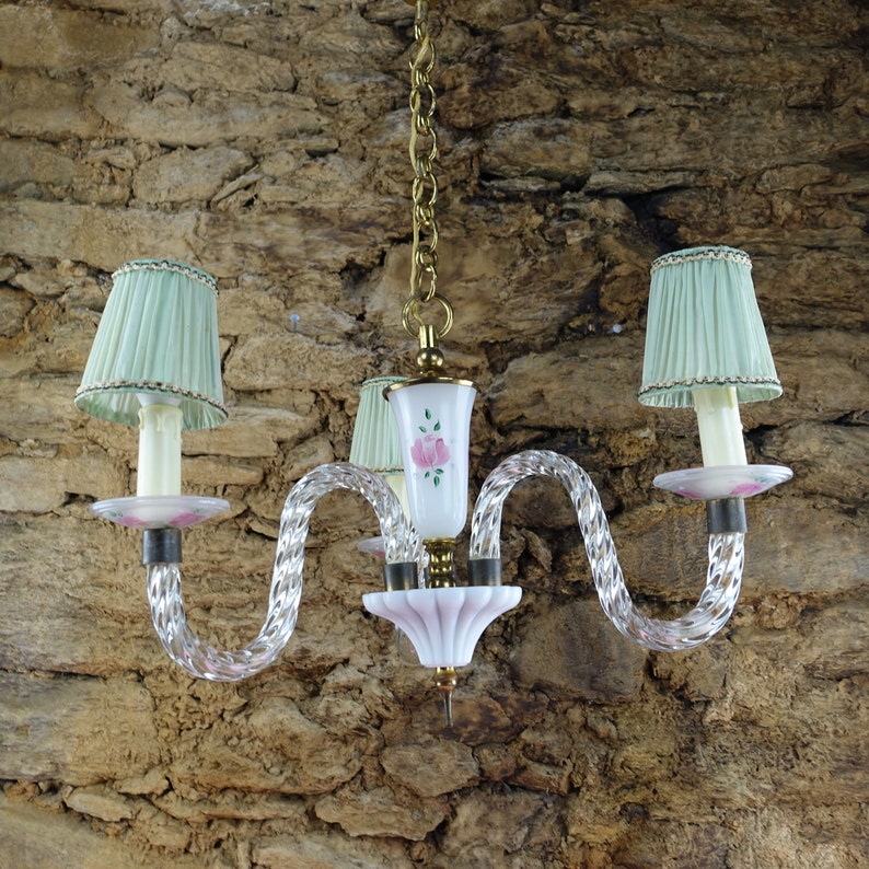 May include: A crystal chandelier with three lights, each with a pale green lampshade. The chandelier has a white and pink glass center piece with a floral design.