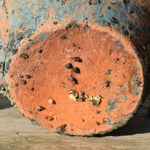 Pu&ograve; includere: Il fondo di un vaso in terracotta con una glassa blu. Il vaso ha una superficie ruvida e testurizzata ed &egrave; ricoperto da piccole macchie marrone scuro.
