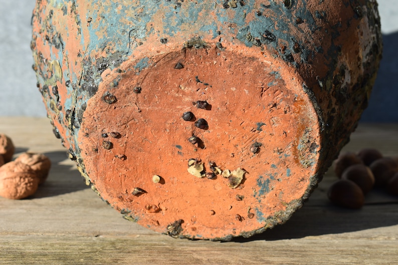 Pu&ograve; includere: Il fondo di un vaso in terracotta con una glassa blu. Il vaso ha una superficie ruvida e testurizzata ed &egrave; ricoperto da piccole macchie marrone scuro.