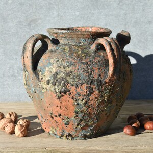 Pu&ograve; includere: Un grande vaso in terracotta rustico con due manici. Il vaso ha una finitura screziata e invecchiata con sfumature di marrone, blu e verde.