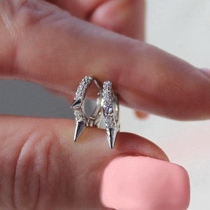 May include: A pair of silver hoop earrings with small, clear stones and pointed spikes.