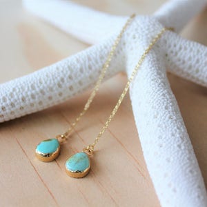 Op de afbeelding: Een paar lange, gouden kettingoorbellen met turquoise druppelvormige stenen.