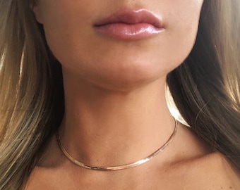 May include: A thin gold chain necklace worn as a choker. The chain is smooth and has a subtle shine.