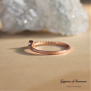 May include: A delicate rose gold ring with a small clear gemstone set in the band. The band is twisted and has a beaded design.