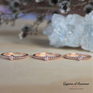 May include: Three rose gold rings with a single pear-shaped clear stone set in each ring. The rings are beaded and have a delicate design.