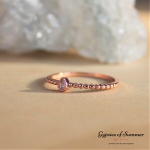 May include: A delicate rose gold ring with a single clear pear-shaped stone set in the center. The band is adorned with small beads.