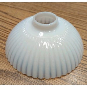 May include: A white, opalescent glass lampshade with a ribbed, scalloped design. The shade has a rounded, dome-like shape with a small, cylindrical opening at the top. The glass has a glossy finish and a subtle, bluish hue.
