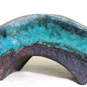May include: A curved ceramic sculpture featuring a vibrant turquoise glazed top surface with a crackled texture. The base and sides are finished in a dark, textured, metallic-toned glaze that contrasts with the bright blue upper section.