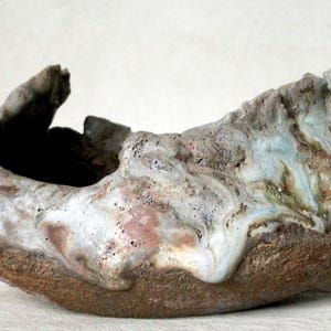 Puede incluir: Una maceta de cerámica con una forma orgánica única y un esmalte moteado en tonos de marrón, blanco y azul. La maceta tiene una boca ancha y abierta y una base profunda y redondeada.