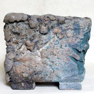 Peut inclure: Un pot de fleurs rectangulaire en céramique avec une surface rugueuse, inégale et texturée. L'extérieur présente une palette de couleurs tachetées de tons terreux marron, gris et bleu sourd, avec un aspect épais et accidenté et deux petits pieds.