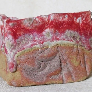 Puede incluir: Un pequeño macetero rectangular de cerámica con un esmalte texturizado marrón rojizo. El macetero tiene una forma única, irregular y un borde ligeramente elevado.