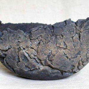 May include: A dark brown, hand-formed ceramic bowl with a highly textured, cracked, and uneven surface. The exterior features a rugged, earth-toned finish with deep fissures and a jagged, irregular rim, showcasing a raw and organic appearance.