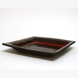 May include: A square ceramic dish with a dark brown rim and a red interior. The dish is glazed and has a glossy finish.