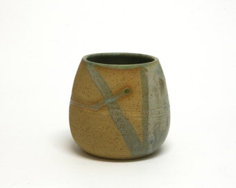 Ceramic bowl with soft blue, gray, and green colors beside large areas of exposed brown raw material. Handmade gift.