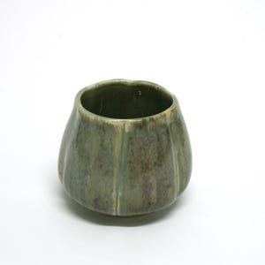 May include: A small, green ceramic cup with a textured, rippled surface. The cup has a rounded shape and a wide opening.