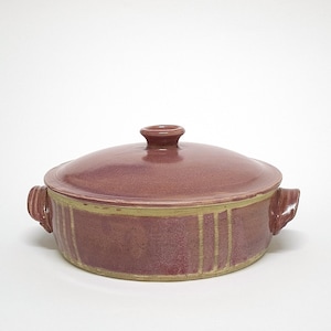 May include: A round ceramic casserole dish with a matching lid, featuring a dusty rose glaze and contrasting tan vertical stripes along the sides. The vessel includes two small side handles and a central knob on the lid for easy lifting.