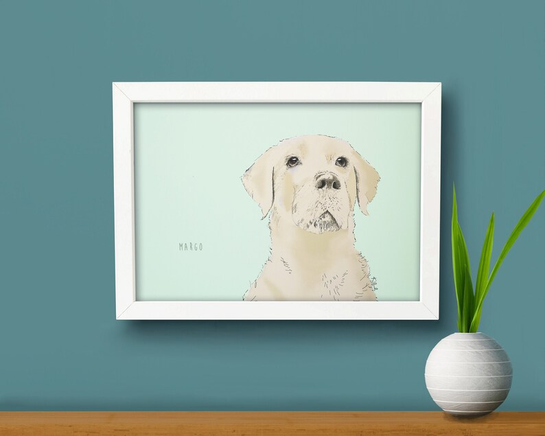 May include: A white framed print of a dog with the name 'MARGO' printed below the image. The dog is a light brown labrador retriever with a light green background.
