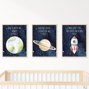 Puede incluir: Tres impresiones de acuarela con ilustraciones de temática espacial y versículos bíblicos inspiradores. La primera impresión presenta una Tierra azul y verde con el texto "Dios está conmigo siempre". La segunda impresión presenta un planeta amarillo y marrón con anillos y el texto "Dios tiene grandes planes para mí". La tercera impresión presenta un cohete rojo y blanco con el texto "No temeré porque Dios está conmigo".