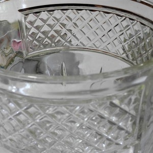 May include: A clear glass cup with a diamond pattern. The cup has a gold rim and is made of thick glass.