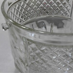 May include: A clear glass ice bucket with a diamond pattern. The bucket has a handle on each side.