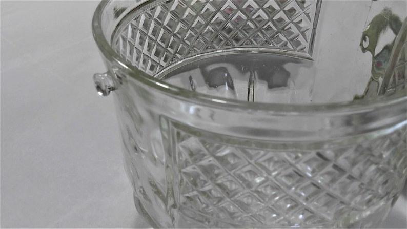 May include: A clear glass ice bucket with a diamond pattern. The bucket has a handle on each side.