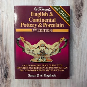May include: A book titled "Warman's English & Continental Pottery & Porcelain 3rd Edition" with a decorative pottery image. The cover is burgundy with gold lettering and a gold horizontal stripe. The book is an illustrated price guide with histories and references.