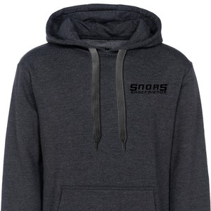 Könnte beinhalten: Dunkelgrauer Kapuzenpullover mit Fronttasche und Kordelzug. Der Text "SNORS SHOEFRIENDS" ist in Schwarz auf der oberen Brust aufgedruckt. Der Pullover hat eine Kapuze und lange Ärmel.